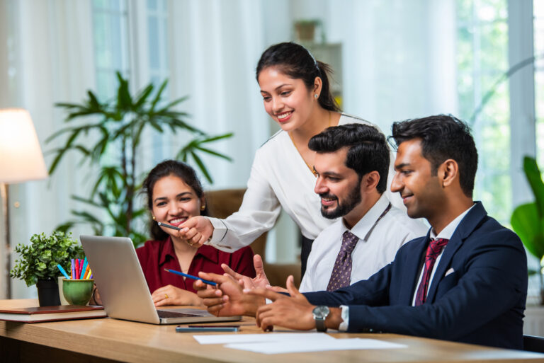 Young Indian asian leader coach teaching employees group analyzing online project explaining business strategy speaking training diverse corporate team with laptop using computer at office meeting